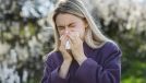 blonde woman blowing nose outside, dealing with side effects of seasonal allergies