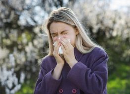 blonde woman blowing nose outside, dealing with side effects of seasonal allergies