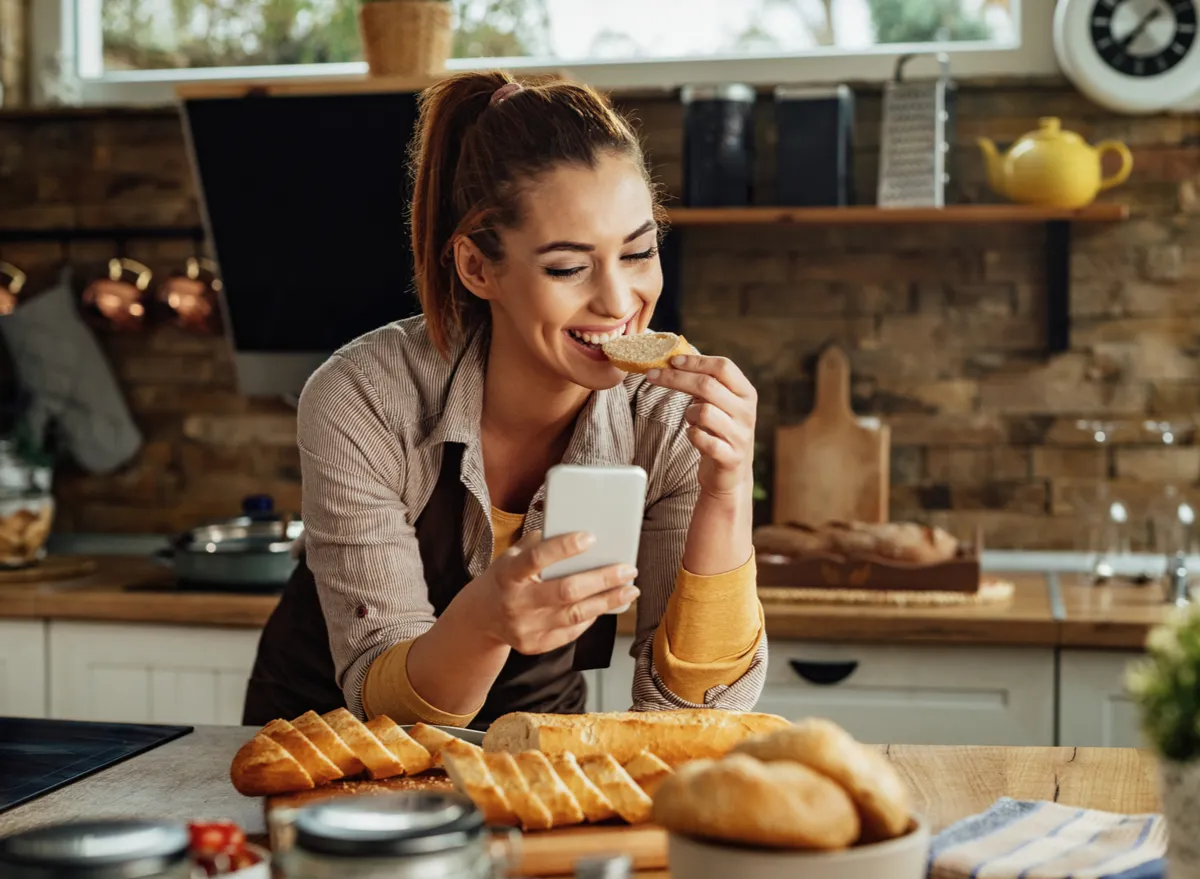 woman eating bread and holding phone