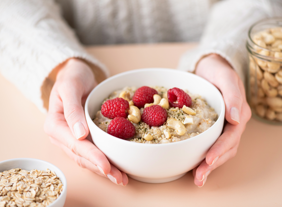 woman holding oatmeal with raspberries, seeds, and nuts