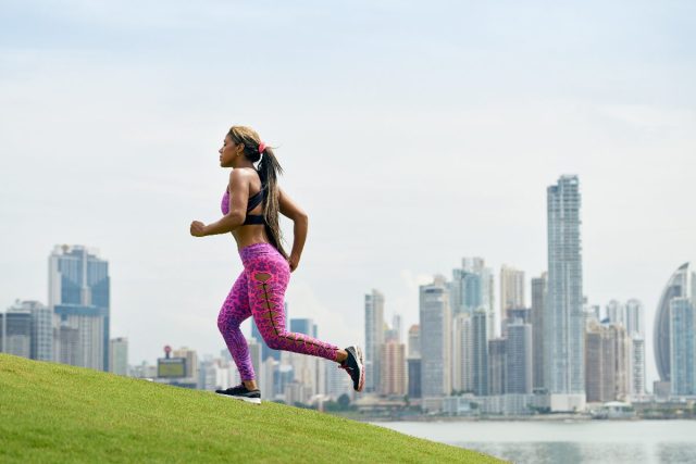 woman jogging uphill to burn double calories, sunny day with city background