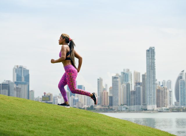 woman jogging uphill to burn double the calories, sunny day with city backdrop