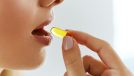 Young Woman Taking Yellow Fish Oil Pill.