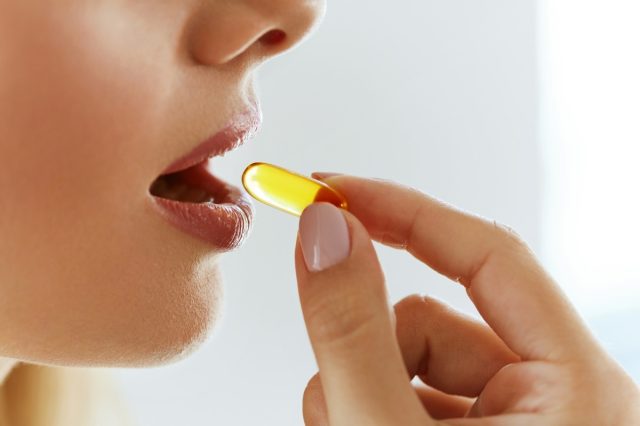 A young woman takes a yellow fish oil pill.