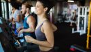 woman performing treadmill cardio workout in gym with friends