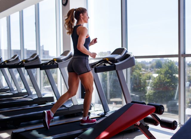 woman doing fat-burning workout on treadmill in front of windows at gym