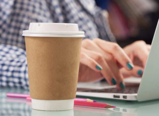 woman typing disposable next to disposable coffee cup