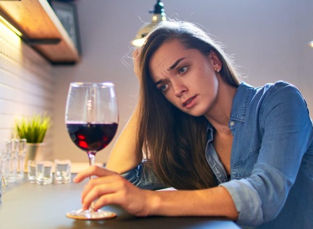 Sad woman drinking wine at kitchen.