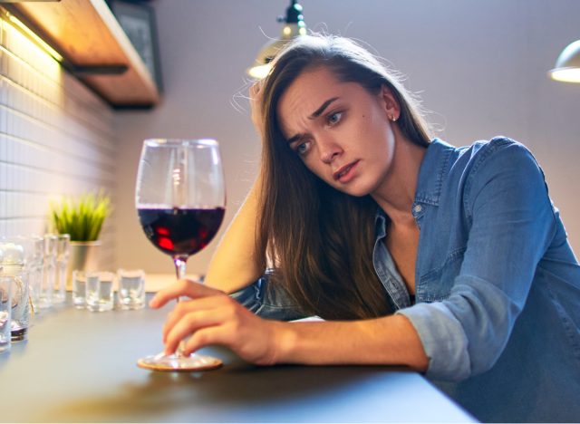 Sad woman drinking wine at kitchen.
