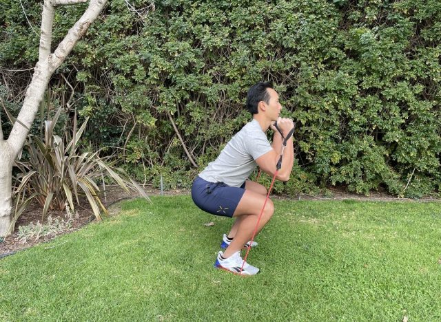 trainer performing band squat, exercise to make body look 10 years younger