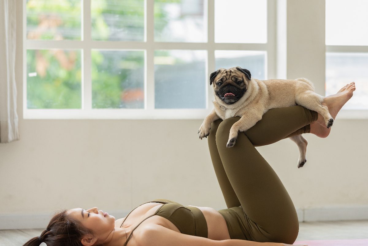 woman doing dog yoga with her pup, exercises to do with your dog indoors in the summer