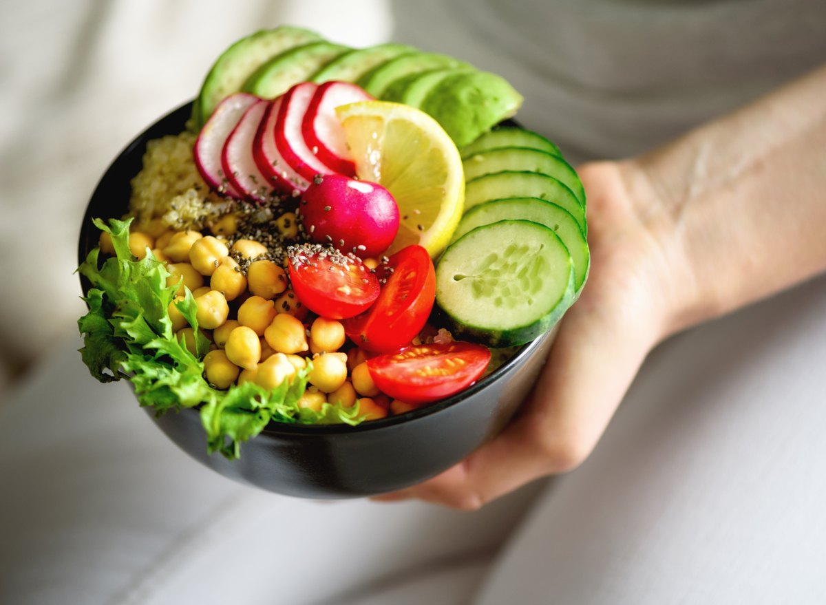 holding plant-based bowl with veggies, chickpeas, tomatoes, chia seeds, and lemon