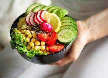 holding plant-based bowl with veggies, chickpeas, tomatoes, chia seeds, and lemon