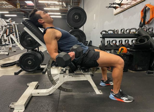 The trainer performs the incline dumbbell bend