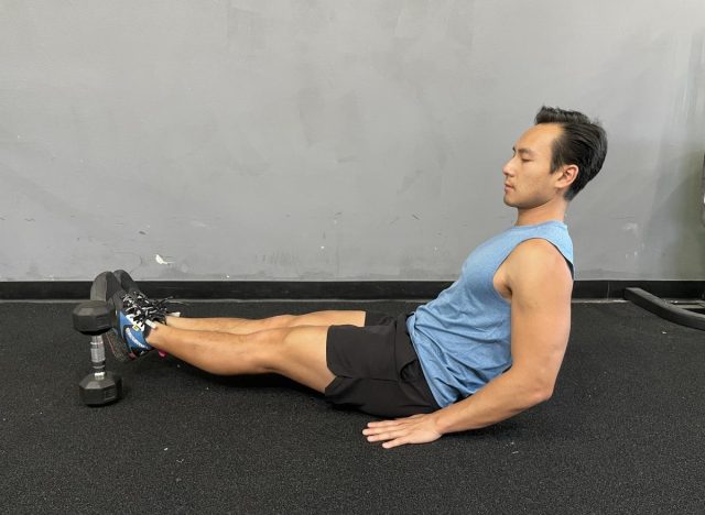 trainer demonstrating leg lifts over dumbbell to shrink belly fat faster