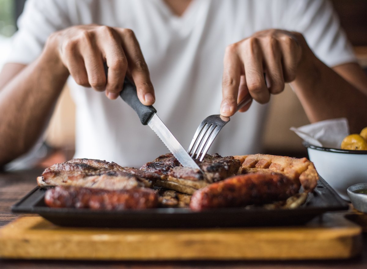 Есть мясо с ножа. Человек ест стейк в ресторане. Жареное мясо.
