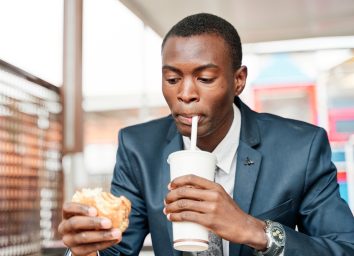 man drinking soda and holding burger
