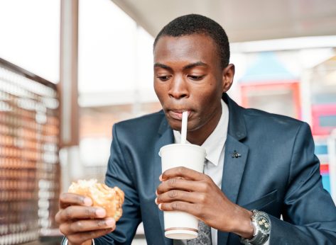 man drinking soda and holding burger