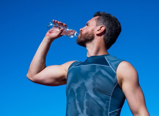 Homme sportif buvant de l'eau à l'extérieur le jour d'été ensoleillé