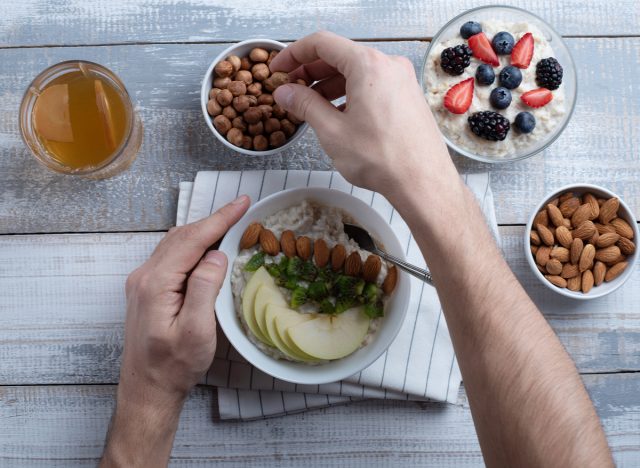 man preparing oatmeal bowl with fruit and nuts