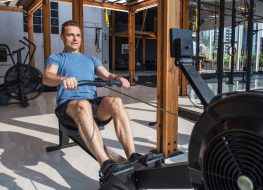 man demonstrating rowing machine exercise to lose your gut in your 40s