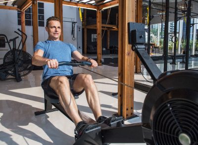 man demonstrating rowing machine exercise to lose your gut in your 40s
