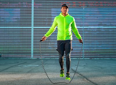 man in bright green outfit performing weighted jump rope workout