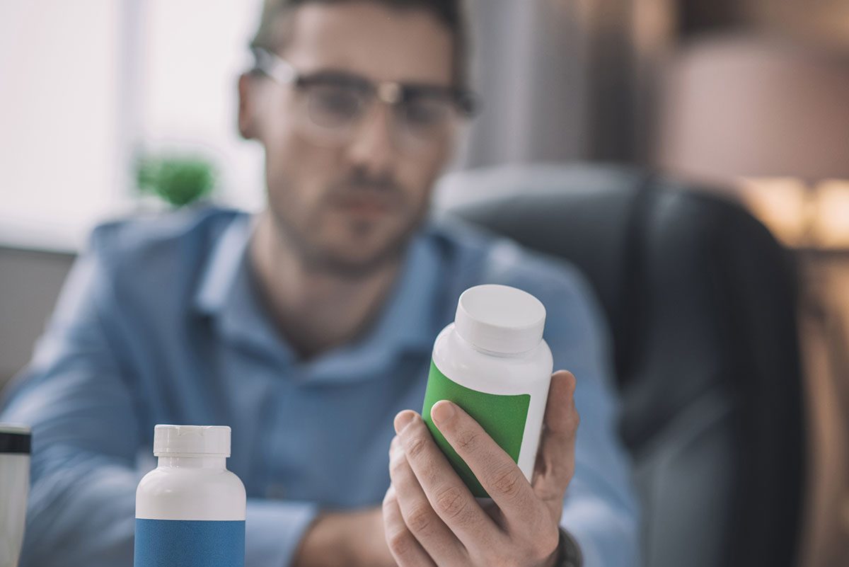 Hesitations.,Bearded,Man,In,Blue,Shirt,Looking,Hesitated,While,Choosing, Pills, bottle