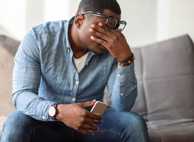 Feeling exhausted. Frustrated young black man massaging his nose and keeping eyes closed while sitting at his working place in office