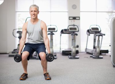 man in his 50s doing squats with dumbbells to get rid of a pot belly
