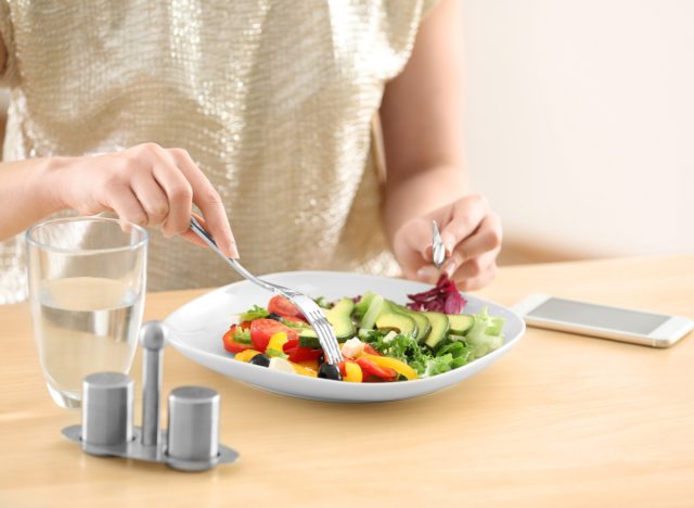 vrouw die salade, waterglas en telefoon op tafel eet