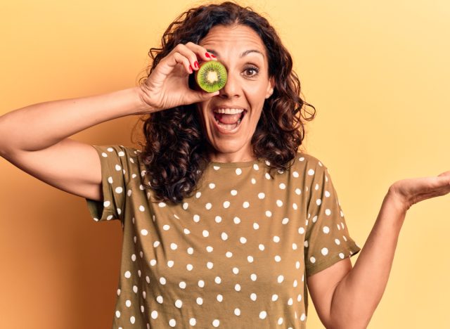 woman holding kiwi over eye
