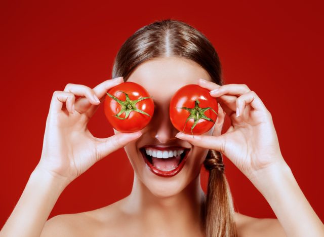 woman holding tomatoes over her eyes and smiling
