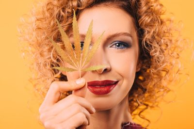 Portrait of a curly woman with a leaf of marijuana in her hand. Face close-up on a yellow background. Legalization of drugs