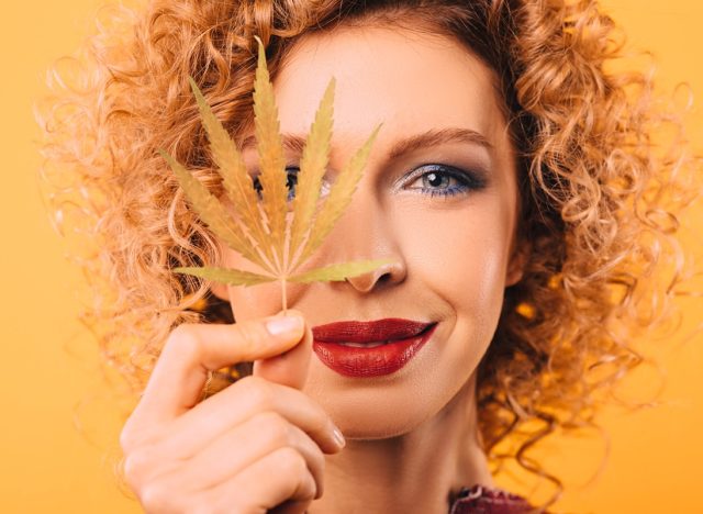 Portrait of a curly woman with a leaf of marijuana in her hand. Face close-up on a yellow background. Legalization of drugs