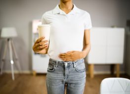 Woman with coffee cup, holding stomach