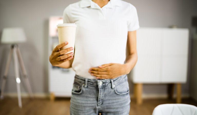 Woman with coffee cup, holding stomach