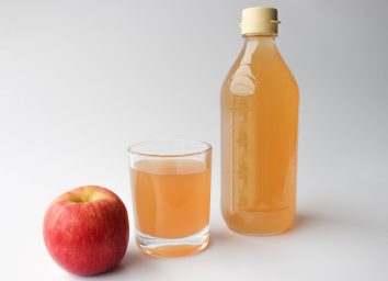 apple cider vinegar in a bottle and glass next to an apple