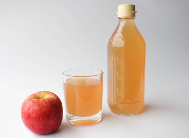 apple cider vinegar in a bottle and glass next to an apple