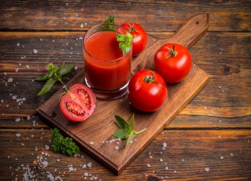 glass of tomato juice and tomatoes on wooden cutting board
