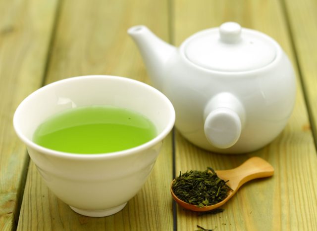 té verde en taza y tetera y hojas de té en cuchara de madera