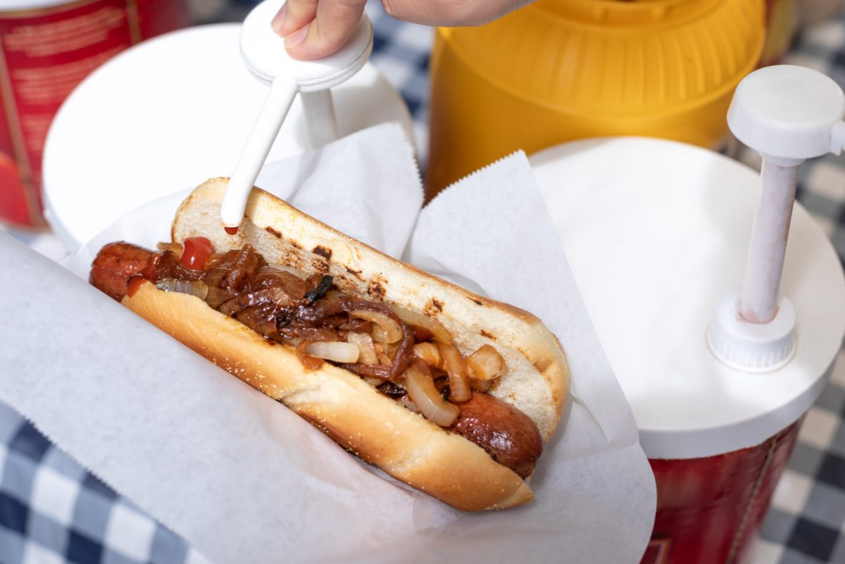 ketchup being pumped onto hot dog with grilled onions