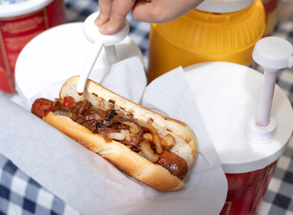 ketchup being pumped onto hot dog with grilled onions