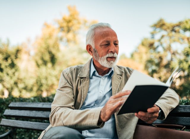 mature man reading a book outdoors, demonstrating how to keep your brain young