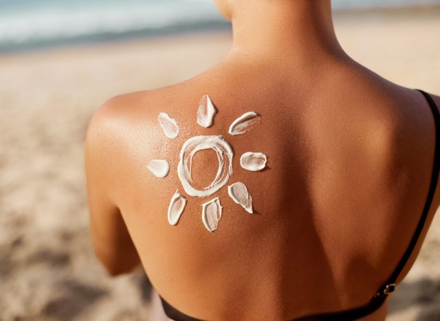 woman sitting on beach with sun drawn in sunscreen on back