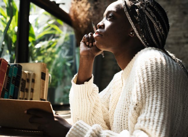 woman pensive journaling, thinking at desk and looking out window