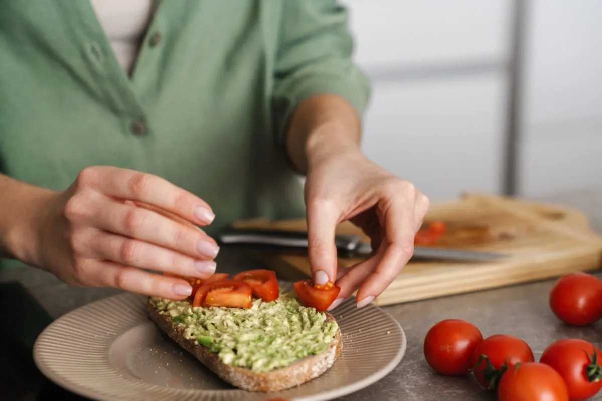 woman placing tomatoes on avocado toast