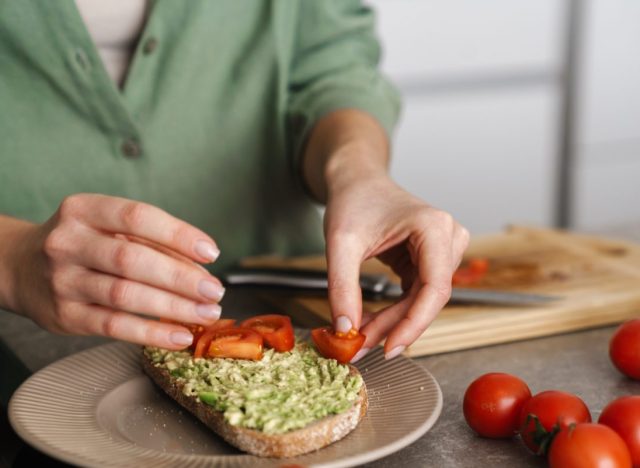 woman placing tomatoes on avocado toast