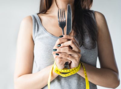 Woman holding silverware with hands wrapped in measuring tape