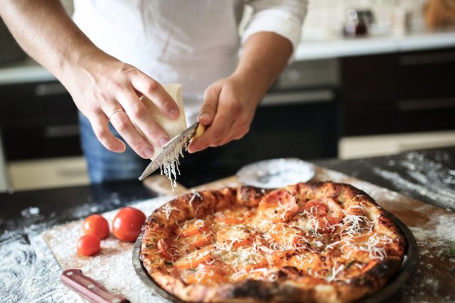 chef grating cheese over pizza